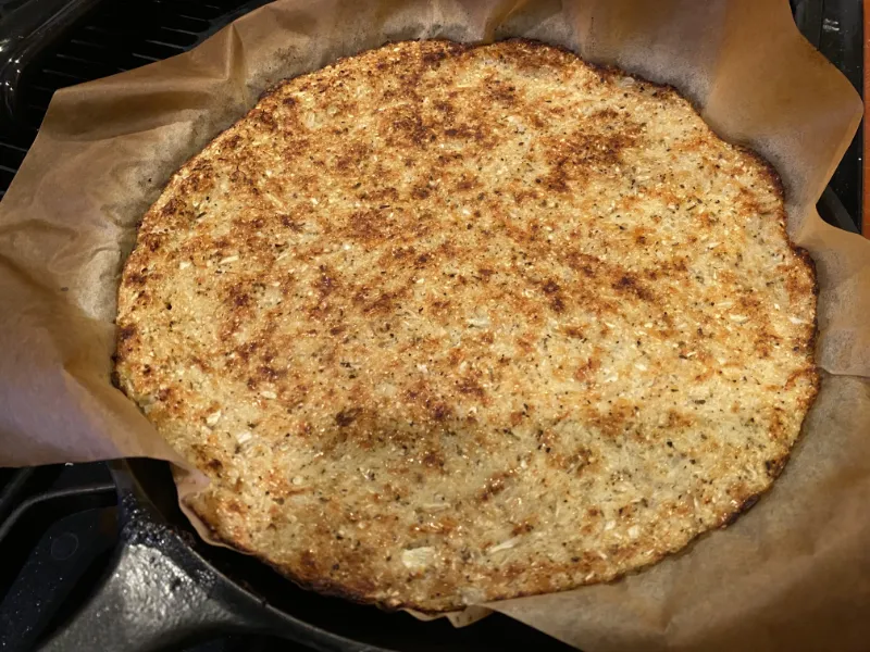 A cooking cauliflower pizza crust after cooking the first side