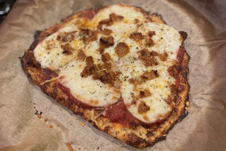 A cooked pizza cooling on parchment paper, made with a cauliflower pizza crust recipe