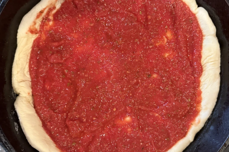 Tavern-style pizza sauce on an uncooked pizza dough, awaiting toppings